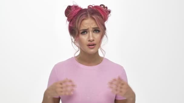 Niezadowolona młoda kobieta z kolorowym różowym fryzurze mówi co z jej rękami podniesionymi na białym tle - Materiał filmowy, wideo