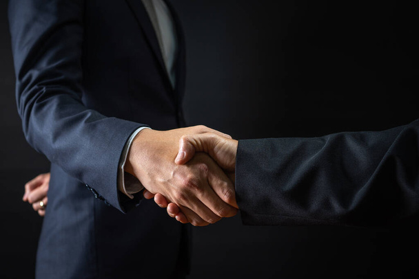 Business agreement and successful negotiation concept, businessman in suit shake hand with customer, client after formal communication and contract deal success on black background  - Foto, afbeelding