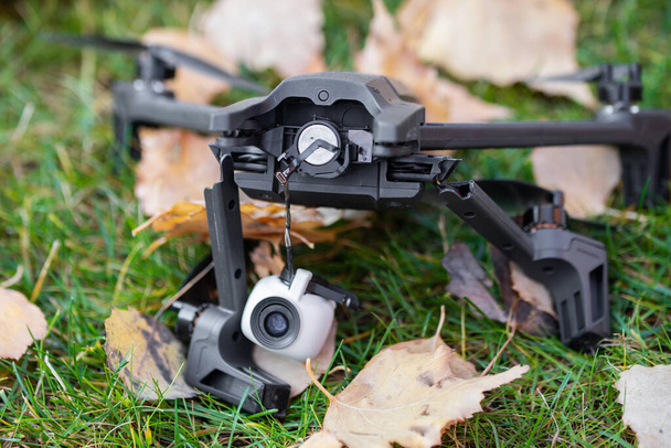 Quadcopter negro roto drone uav acostado en césped de hierba verde en el suelo después de accidente de choque. Fallo de control remoto debido a la fuerte interferencia del viento. Cámara agrietada gimball y piernas de plástico. - Foto, Imagen