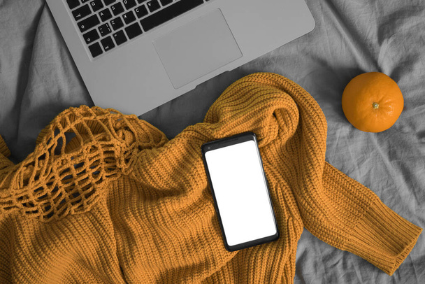 Mobile Phone With Blank Screen On Woolen Sweater Near Orange And Laptop. Copy Space. Empty Space. - Foto, afbeelding