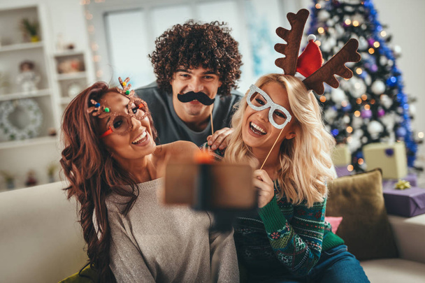 Üç neşeli arkadaş bir dairede güzel vakit geçiriyorlar ve Noel tatilinde selfie çekiyorlar..  - Fotoğraf, Görsel