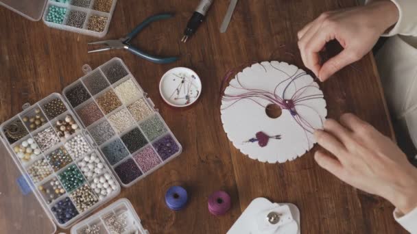Lifestyle-Konzept, Arbeit von zu Hause aus, um das Leben neu zu erfinden: Ansicht von Frauenhänden, die Makrameknoten aus dem Fuchsia-Faden herstellen und einen Ohrring auf Kumihimo-Werkzeugen auf dem Holztisch herstellen - Filmmaterial, Video