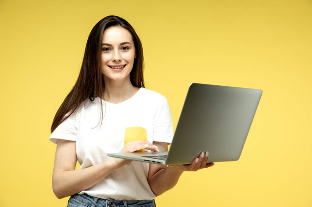 Young beautiful businesswoman with dark short hair in white shirt happily working on laptop over yellow background - Foto, immagini