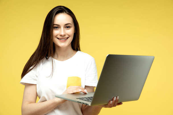 Young beautiful businesswoman with dark short hair in white shirt happily working on laptop over yellow background - Foto, immagini