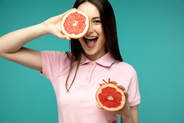 attractive happy model in living coral posing with grapefruit isolated on blue - Photo, Image