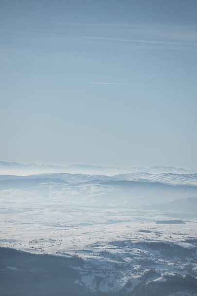 Hermosa vista de la cordillera parcialmente cubierta de niebla y nieve con cielo azul claro
. - Foto, imagen
