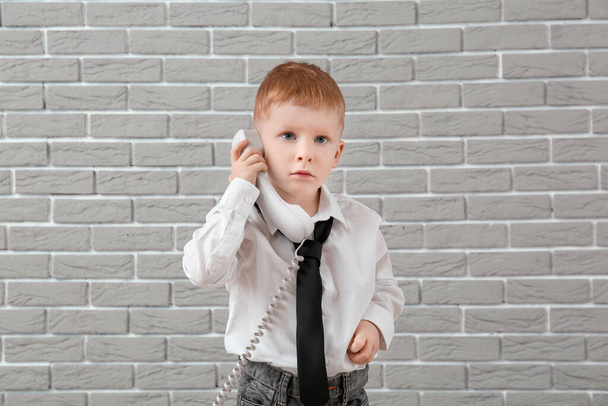 Cute little boy talking by telephone near grey wall - Fotografie, Obrázek
