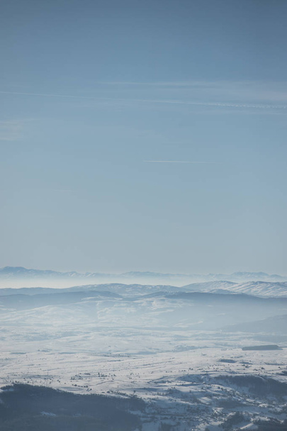 Beautiful view of the mountain range partially covered by fog and snow with clear blue sky. - Photo, Image