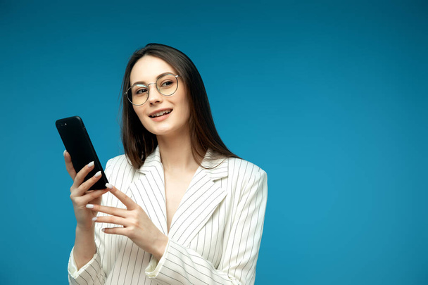 Mladá krásná žena pomocí mobilních telefonů studio na modrou barvu pozadí - Fotografie, Obrázek