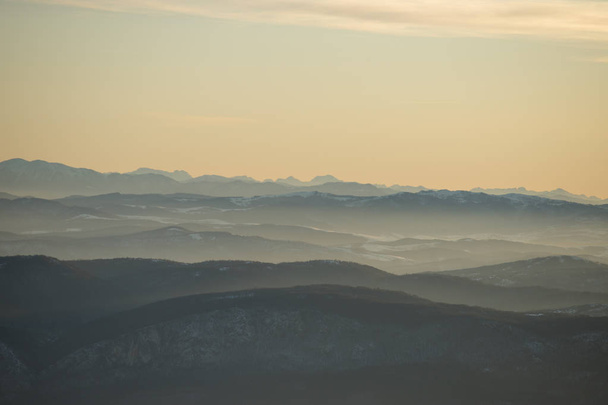 Gyönyörű kilátás nyílik a hegyvonulatra, amelyet részben hó borít napnyugta előtt. Részben narancssárga naplemente ég - Fotó, kép