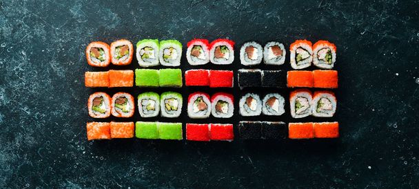Big set of pieces of sushi rolls on black stone background. Top view. Free space for your text. - Foto, Bild
