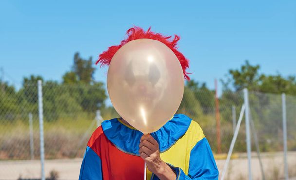 primo piano di un clown spaventoso che indossa un colorato costume giallo, rosso e blu all'aperto, con un palloncino davanti al viso
 - Foto, immagini