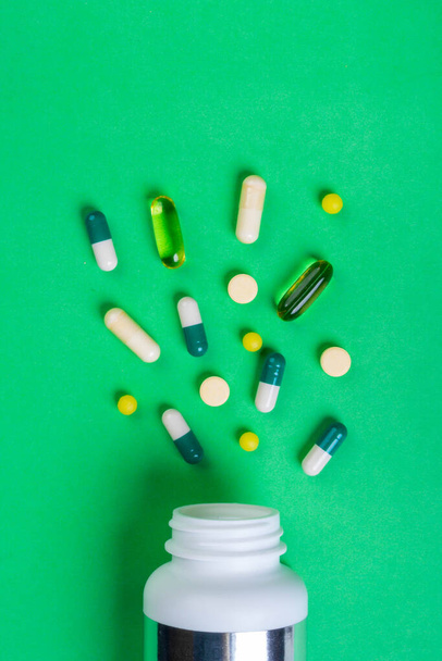 Fehér palack és halom válogatott gyógyszerészeti gyógyszer tabletták, tabletták és kapszulák a zöld háttér - Fotó, kép