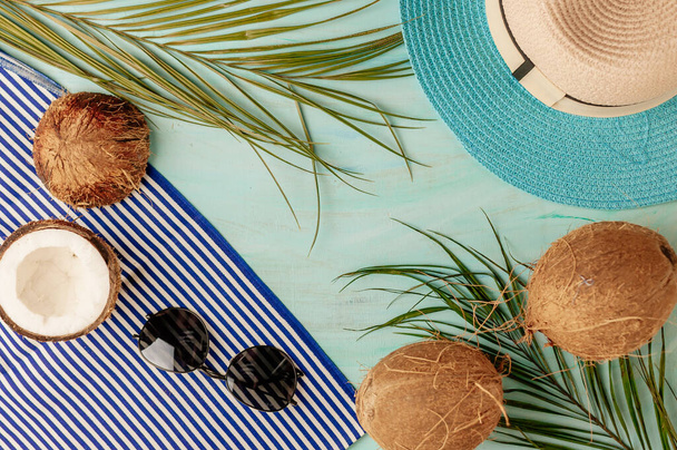 Summer composition or layout. Tropical palm leaves, hat, glasses, beach towel, coconut on a background of sea greens. The concept of the summer season and heat. Flat lay, top view, copy space - Фото, изображение