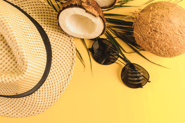 Summer composition. Tropical palm leaves, hat, glasses and broken coconut on a sandy background. The concept of the summer season, parties and heat. Flat lay, top view, copy space - Foto, Imagem