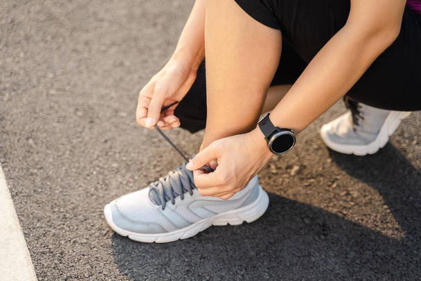 Nahaufnahme einer jungen Läuferin, die ihre Schnürsenkel bindet. Gesundheits- und Fitnesskonzept. - Foto, Bild