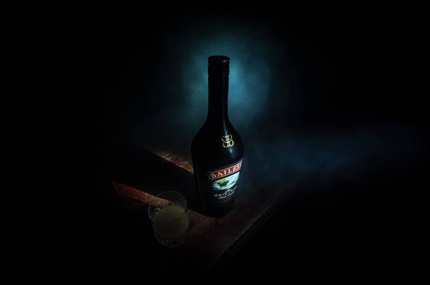 BAKU, AZERBAIJAN - FEB 09, 2020: Baileys Irish Cream is an Irish whiskey- and cream-based liqueur, made by Gilbeys of Ireland. A bottle of liqueur on wooden table with dark toned foggy background. - Foto, afbeelding