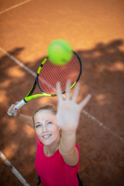 Top view of attractive young woman tennis player serving on a clay tennis court.  - Fotografie, Obrázek