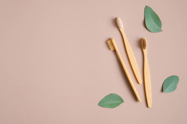 Eco-friendly bamboo toothbrushes and green leaves on brown background. Flat lay, top view. Zero waste, plastic free concept. Sustainable lifestyle. - Фото, изображение
