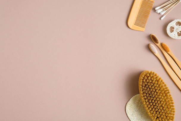 Eco-friendly bath accessories on brown background. Flat lay cotton ear sticks, bamboo toothbrushes, hair comb, bath peeling brush, luffa sponge. Beauty and SPA treatment concept - 写真・画像