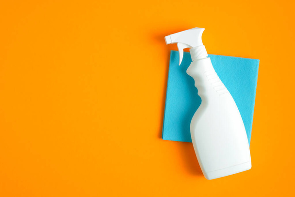Reinigungs-Sprühflasche auf blauer Serviette auf orangefarbenem Hintergrund. Flache Lage, Draufsicht. Konzept der Hausreinigung - Foto, Bild