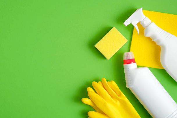 Cleaning equipment set on green background. Top view yellow sponge, rubber gloves, cleaner bottles. Cleaning services concept. - Foto, imagen