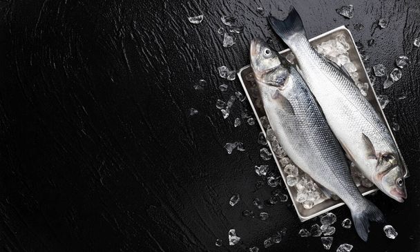 Seabass fish on metal tray on black stone background - Foto, afbeelding