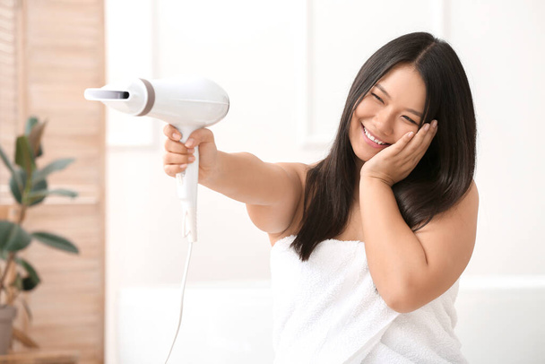 Beautiful Asian woman with hair dryer at home - Photo, Image