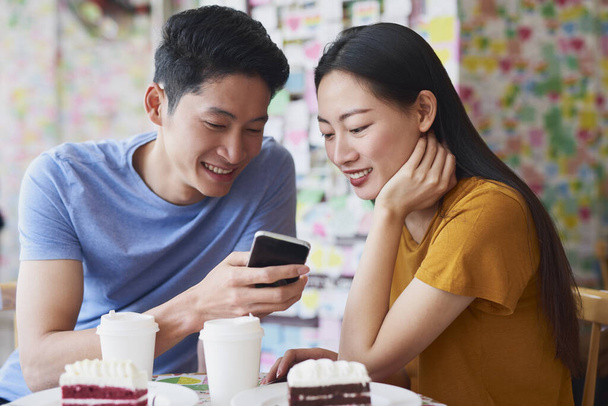 Νεαρό ζευγάρι ελέγχει κάτι στο κινητό τηλέφωνο στο καφέ - Φωτογραφία, εικόνα