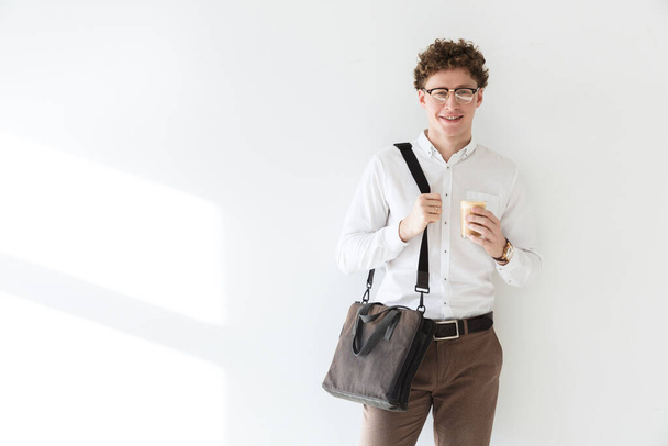 Handsome confident young curly haired businessman wearing white shirt standing infront of isolated background, drinking coffee - Zdjęcie, obraz