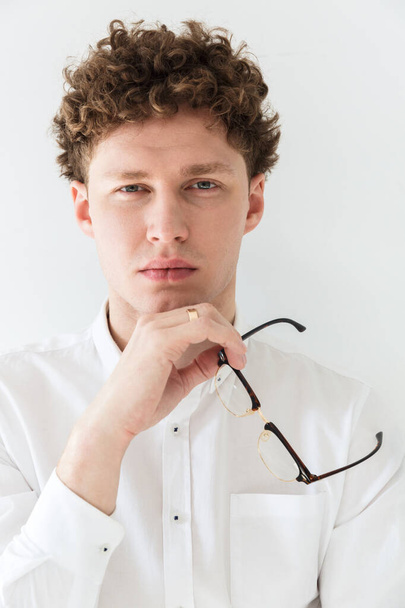 Close up of a handsome confident young curly haired businessman wearing white shirt standing infront of isolated background, posing in glasses - 写真・画像