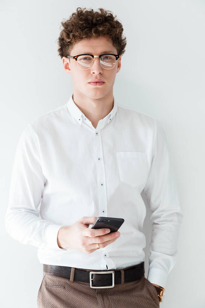 Ritratto di un giovane e attraente uomo d'affari dai capelli ricci di successo in piedi davanti allo sfondo bianco, utilizzando il telefono cellulare
 - Foto, immagini