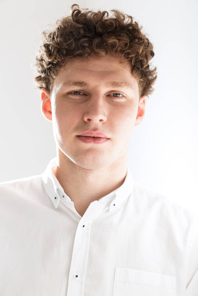 Close up of a handsome confident young curly haired businessman wearing white shirt standing infront of isolated background, posing in glasses - Foto, imagen
