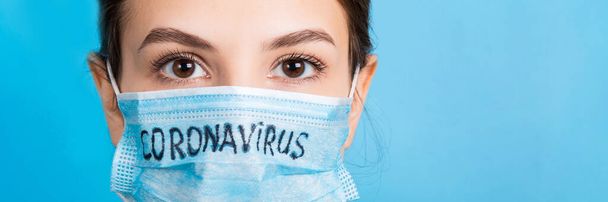 Mavi arka planda Coronavirus metni olan tıbbi maskeli bir kadının portresi. Coronavirus konsepti. Solunum koruması. - Fotoğraf, Görsel