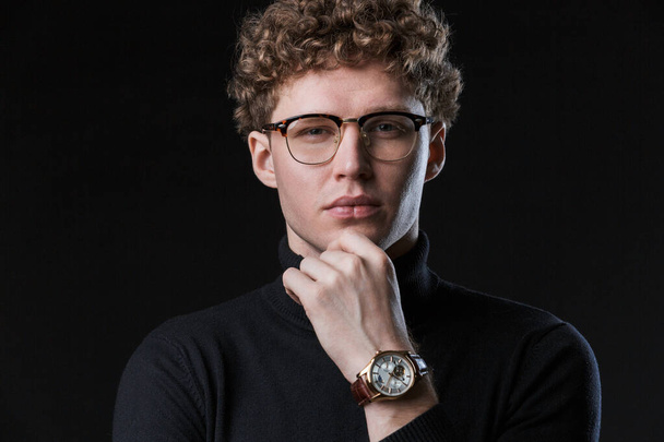 Close up of a handsome confident young curly haired businessman wearing white shirt standing infront of isolated black background, posing in glasses, looking at camera - Foto, imagen