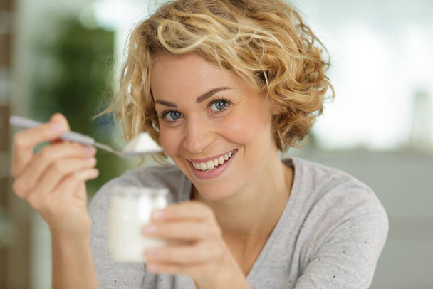 happy young woman eating yogurt in kitchen - Фото, изображение