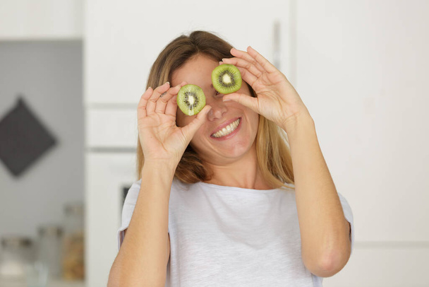 beautiful young woman holding two kiwis on her eyes - Photo, image