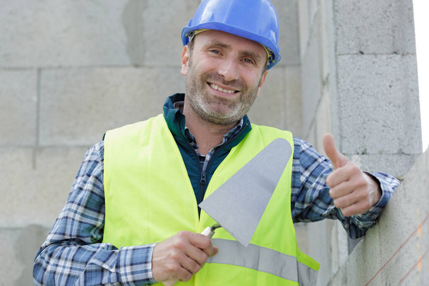 улыбающийся молодой строитель в каске показывает большие пальцы вверх
 - Фото, изображение