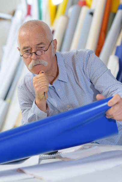 senior worker looking at roll of blue vinyl material - Photo, image
