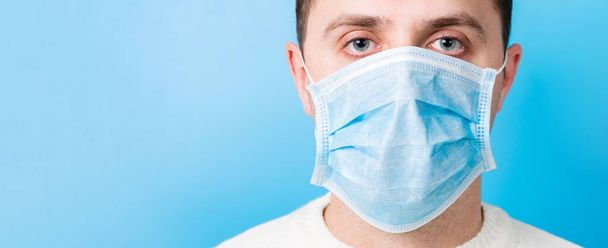Portrait of young man wearing medical mask at blue background. Coronavirus concept. Respiratory protection. - Photo, Image