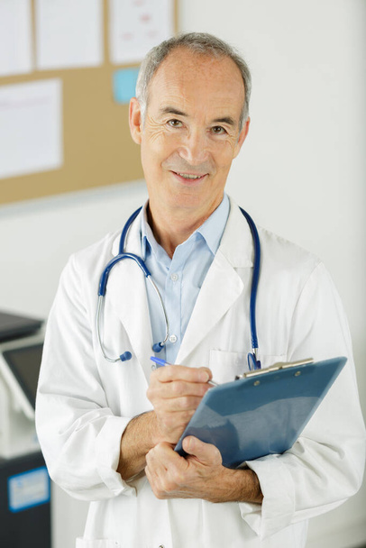 friendly senior doctor holding clipboard - Foto, afbeelding