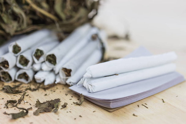 Nahaufnahme von Cannabis-Joints auf hölzernem Hintergrund und auf weißem Papier, das zum Rollen bereit steht. Selektiver Fokus. - Foto, Bild
