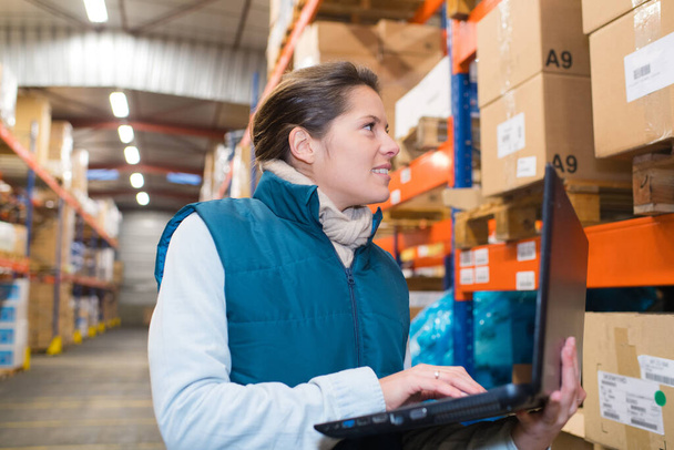 business woman typing on her laptop in a warehouse - Photo, image