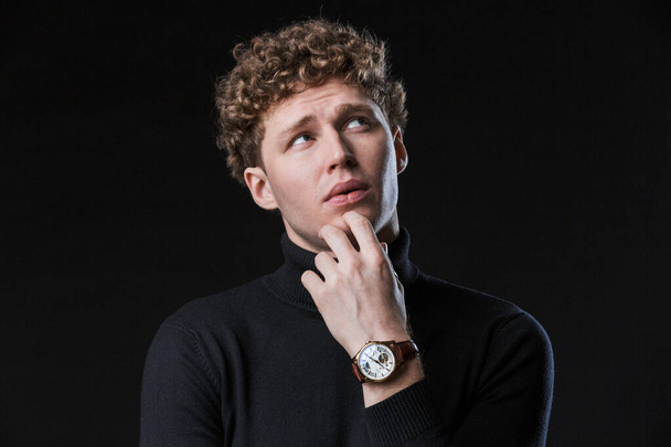 Close up of a handsome confident young curly haired businessman wearing turtleneck standing infront of isolated black background, posing in glasses - Photo, image