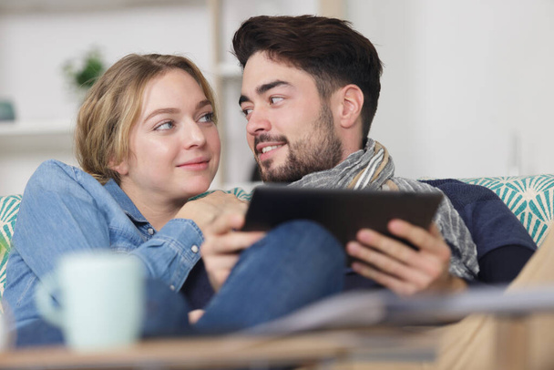 happy couple with digital tablet hugging on sofa at home - Fotografie, Obrázek