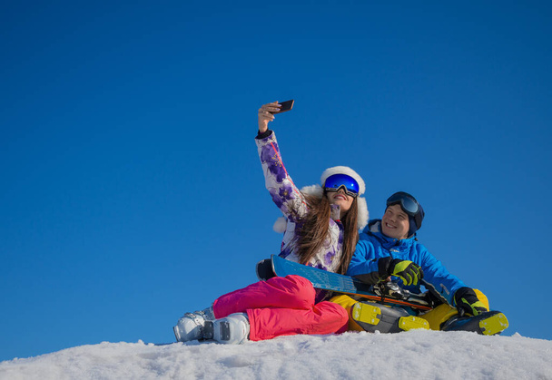 Vidám fiatal szerelmespár, akik téli szelfit készítenek egy hegycsúcson egy síközpontban töltött nyaralás alatt.. - Fotó, kép