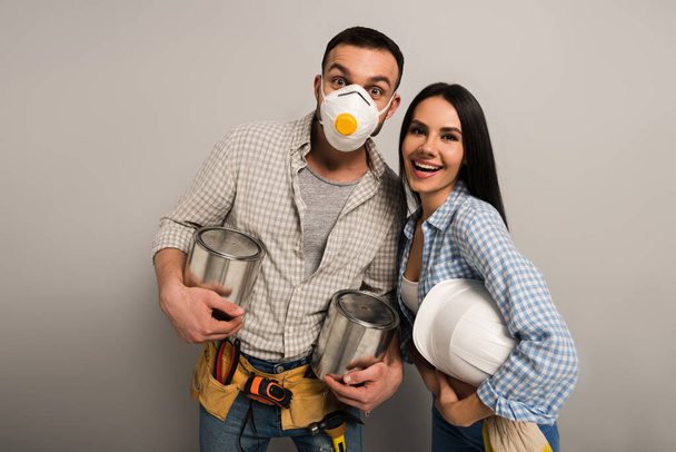 excited manual workers in safety mask holding paint cans and helmet on grey  - Photo, Image