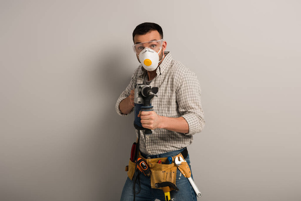 emotional foreman in safety mask holding electric drill on grey - Fotografie, Obrázek