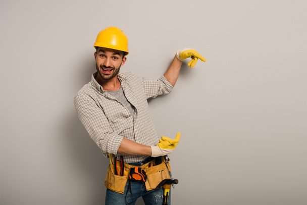 trabajador manual excitado en hardhat y guantes de seguridad apuntando en gris
  - Foto, imagen