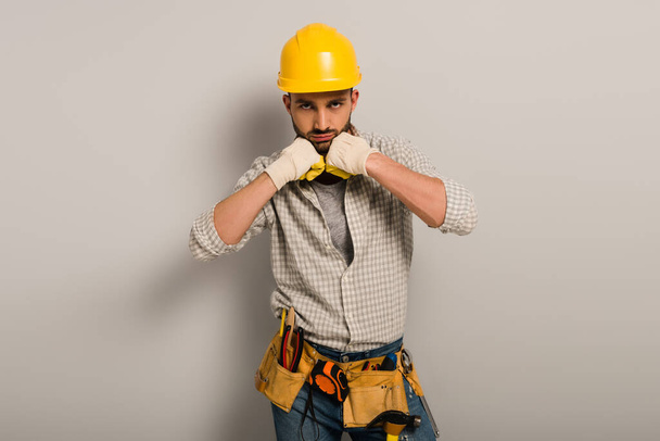 handsome workman in hardhat and gloves with tool belt on grey   - Photo, Image